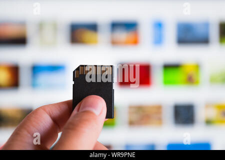 male hand holds memory card against image gallery blurred background. Stock Photo