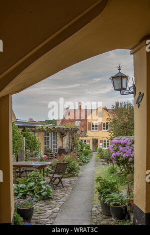 A gateway and a path through a grden full of flowers leading up to a yellow house with an open door. Svendborg, Denmark,  July 10, 2019 Stock Photo