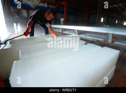 A Chinese worker moves newly-manufactured ice blocks at an ice factory on a scorcher in Liuhe Town, Taicang City, east China's Jiangsu Province, July Stock Photo