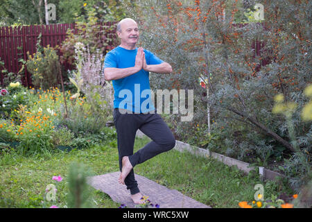 Senior hispanic man standing in tree yoga pose in garden. Balance asana full length Stock Photo