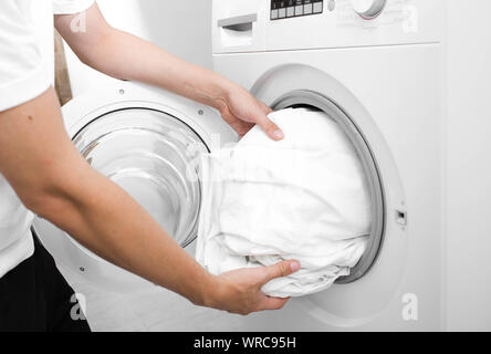 Close up of male hand putting a cloth into washing machine.Wash Linen Bedding Stock Photo