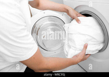 Close up of male hand putting a cloth into washing machine.Wash Linen Bedding Stock Photo