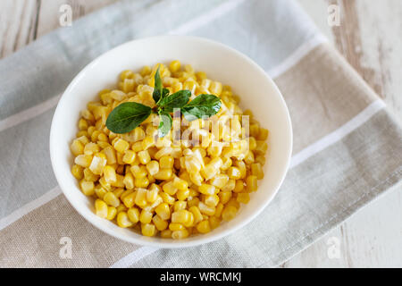 Canned sweet corn in a white bowl on napkin wooden table background. Stock Photo