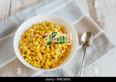 Canned sweet corn in a white bowl on napkin wooden table background. Stock Photo