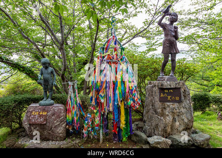 Nagasaki, Japan - 11 July 2019 - Young boy and girl with bird's statues stand next to colorful origami cranes near Nagasaki Atomic Bomb Museum on July Stock Photo