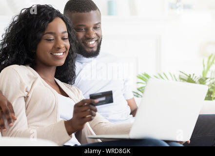 Online Shopping. Happy Black Couple Using Laptop And Credit Card Stock Photo