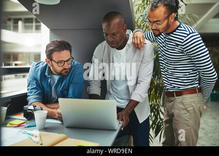 Focused group of diverse creative professionals working together on a laptop in an office meeting pod Stock Photo