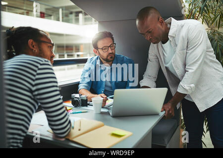 Group of diverse creative professionals working together on a laptop while sitting in an office meeting pod Stock Photo