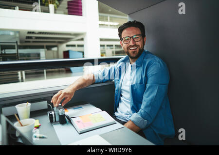 Laughing creative professional going over notes and working on a laptop while sitting alone in an office pod Stock Photo