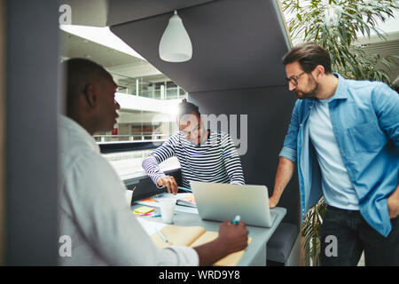 Diverse group of focused businessmen going over notes together while working in an office meeting pod Stock Photo