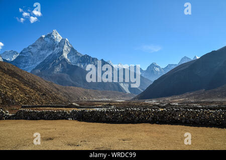 Field looking over a stone fence and the Himalayan mountains Stock Photo