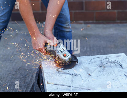 Woman separates metal with a cut-off wheel. One-handed angle grinder. Flex of concrete Stock Photo