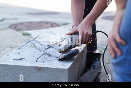 Woman separates metal with a cut-off wheel. One-handed angle grinder. Flex of concrete Stock Photo