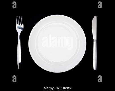 Place setting, white plate, knife and fork, from above on a black background Stock Photo