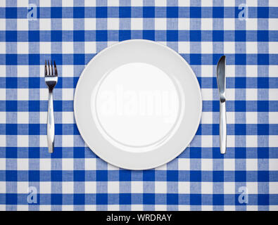 Place setting, round white plate, knife and fork, from above on a blue gingham tablecloth Stock Photo