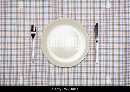 Place setting, white plate, knife and fork, from above on a pastel check tablecloth Stock Photo