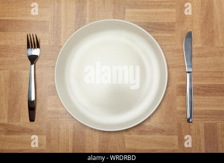 Place setting, white plate, knife and fork, from above on a wooden tabletop Stock Photo