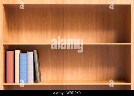 Shelves (one empty) of a wooden bookcase with a few hardback books with blank spines Stock Photo
