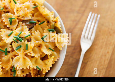 Bowl of cooked Farfalle pasta or bow-tie pasta in a fresh pesto sauce with chopped chives, close up Stock Photo