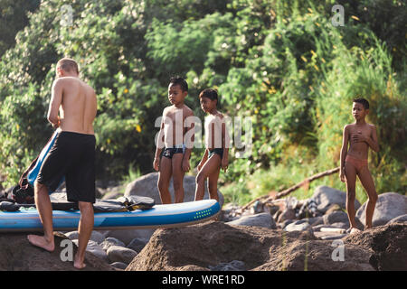 Asian boys looking at surfboard near river Stock Photo