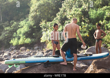 Asian boys looking at surfboard near river Stock Photo