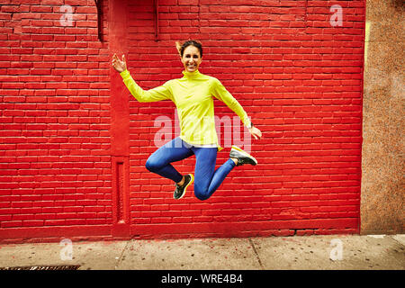 A woman in athletic clothing jumps in front of a vibrant red wall. Stock Photo