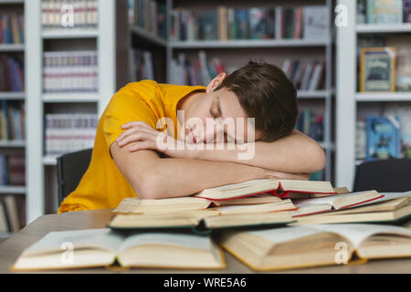 Tired young guy napping on books in library Stock Photo