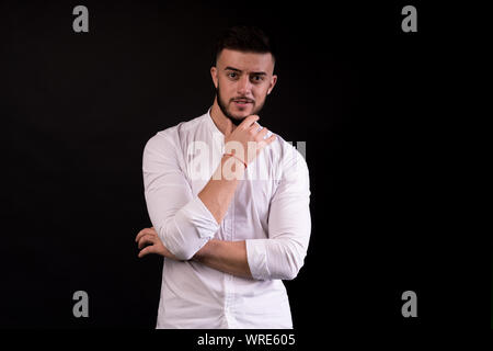 Portrait of the young thinking man looks up with hand near face - isolated on black. Handsome man, focuses on the camera. Stock Photo
