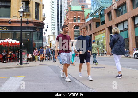 Two young men dressed in shorts and t-shirts walk along Yonge Street in Toronto in September 2019 Stock Photo