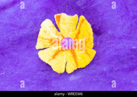 Yellow felt flower on purple dyed raw wool background Stock Photo