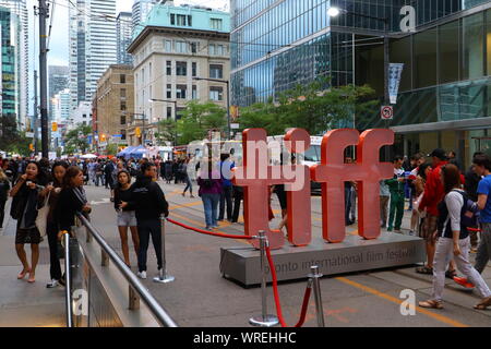 TIFF 2019 fans walk on King St West in Toronto next to the TIFF sign. Stock Photo