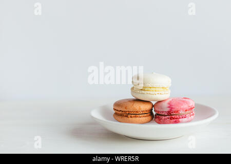 Three French macarons on a white plate. Multicolored macarons. Minimal concept, place for text. Stock Photo
