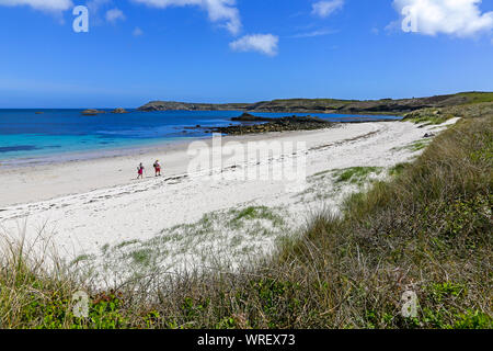 2 people walking on an almost deserted beach at Great Bay in St Martin's Bay, St. Martin’s Island, Isles of Scilly, Cornwall, England, UK