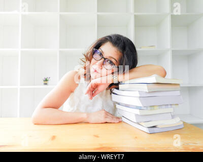 Beautiful women in glasses crushed on the table by a lot of books, very stressed of the study. Stock Photo