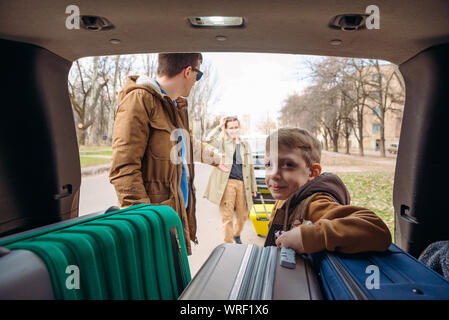 family with kid putting bag in car trunk Stock Photo