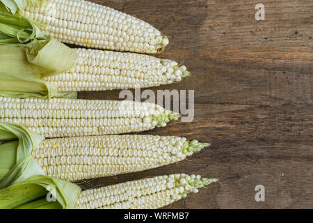 Fresh white corn cobs on old wooden background with place for text. High angle view. Stock Photo