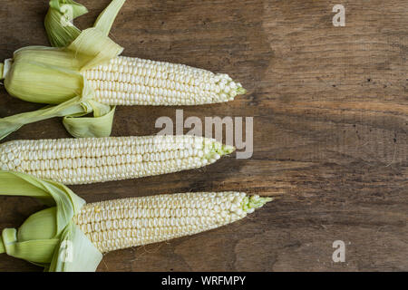 Fresh white corn cobs on old wooden background with place for text. High angle view. Stock Photo