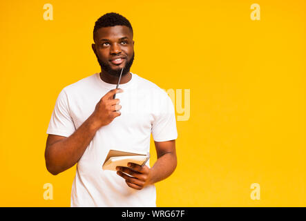 Pensive african guy taking notes, writing check list in notebook Stock Photo