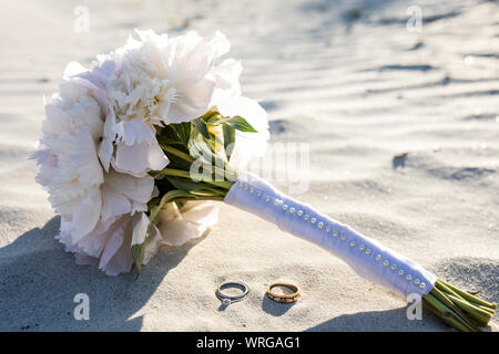Wedding rings and bouquet of peonies on the beach. Stock Photo