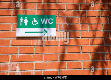 Plaque indicating the direction of disabled toilets on a brick wall. Stock Photo