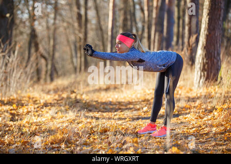 Young fitness woman doing stretching before jogging in autumn park Stock Photo