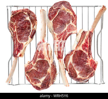 Top view of four frenched bone in veal tomahawk chops dry aging on a stainless steel rack. Stock Photo