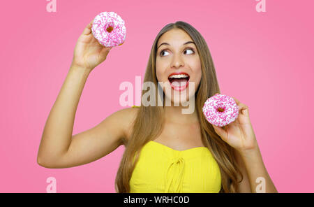 Pretty beautiful young girl playing with donuts looking to the side on pink background. Stock Photo