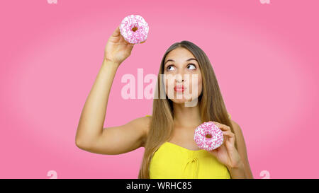 Pretty beautiful young girl playing with donuts looking up on pink background. Stock Photo