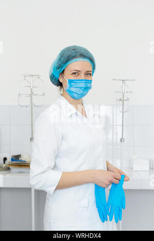 Nurse in scrub and mask puts gloves on her hands. Stock Photo