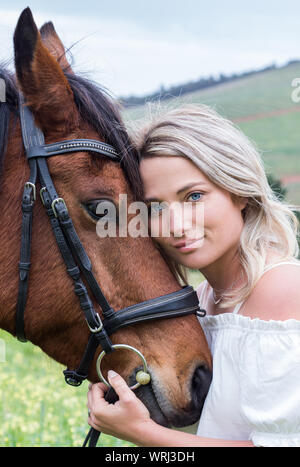 Closeup portrait of a woman with her chestnut Arab horse standing with their faces together, outdoors. Stock Photo