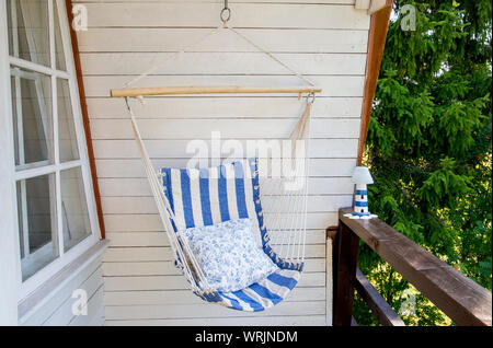 Blue and white striped pattern string and cotton hammock hanging chair, white painted wooden board background. Relaxing in countryside home garden bal Stock Photo