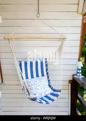 Blue and white striped pattern string and cotton hammock hanging chair, white painted wooden board background. Relaxing in countryside home garden bal Stock Photo