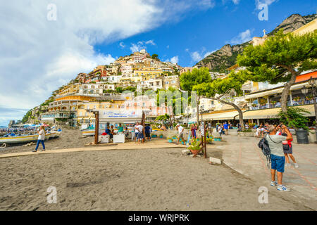 Tourists walk the boardwalk and sandy beach, cafes and shops at the coastal town of Positano Italy on the Amalfi Coast of the Mediterranean Sea