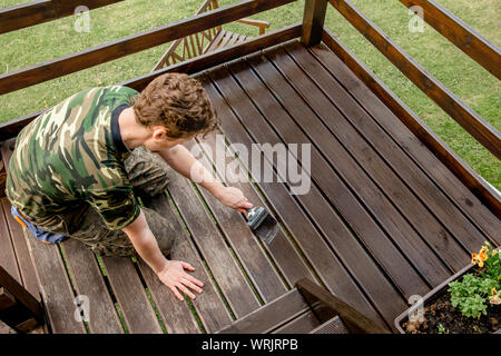 Top view of young man staining garden terrace wooden boards outdoors in spring. Terrace wood stain concept. Stock Photo